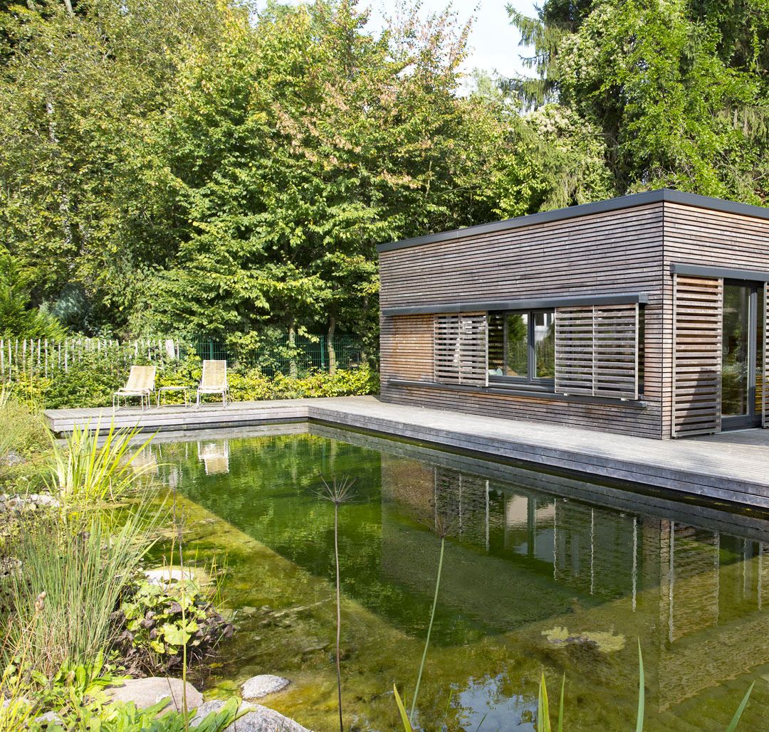 Naturpool mit moderner Holzstruktur Ein Naturpool mit klaren Wasser im Garten und einem modernen Sauna-Holzgebäude im Hintergrund.